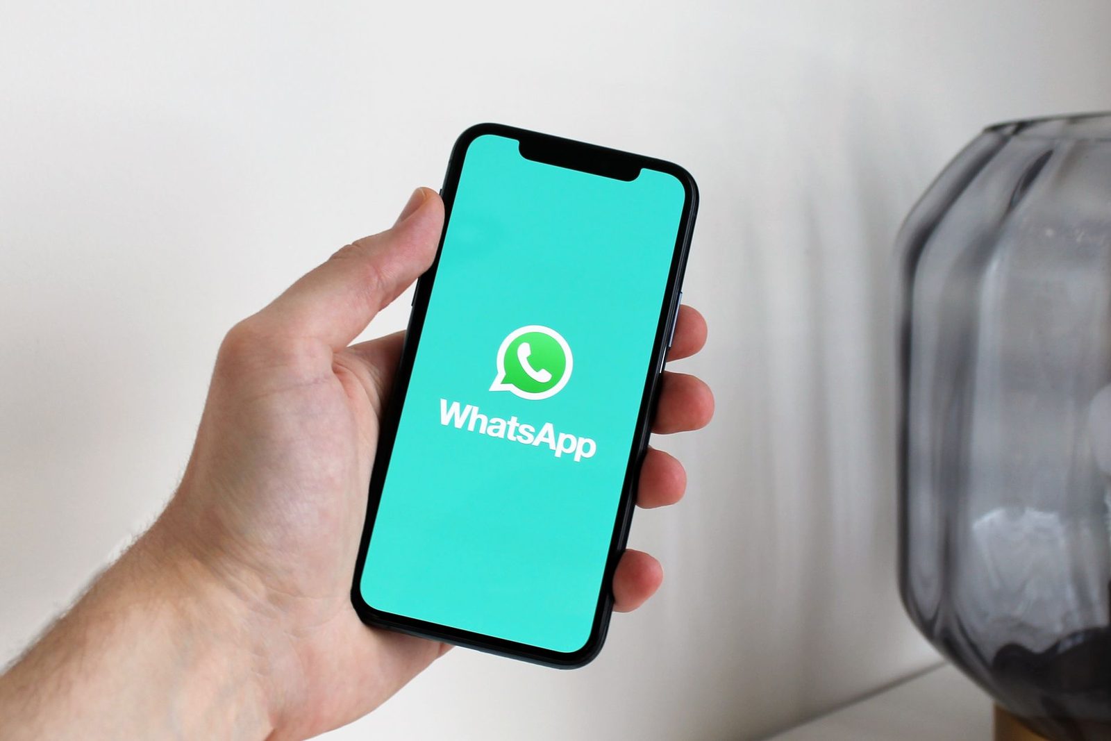Main tenant un smartphone affichant l'écran de démarrage de l'application de messagerie WhatsApp
