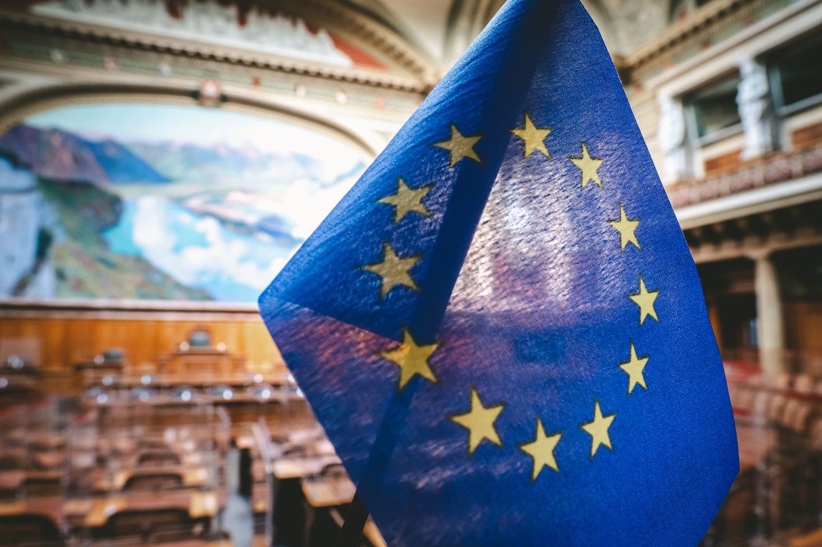 Piccola bandiera dell'Unione europea in primo piano davanti a un'aula parlamentare sfocata