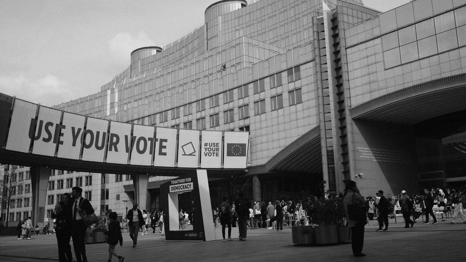 Edificio del Parlamento europeo a Bruxelles con uno striscione «Use your vote» e alcuni passanti