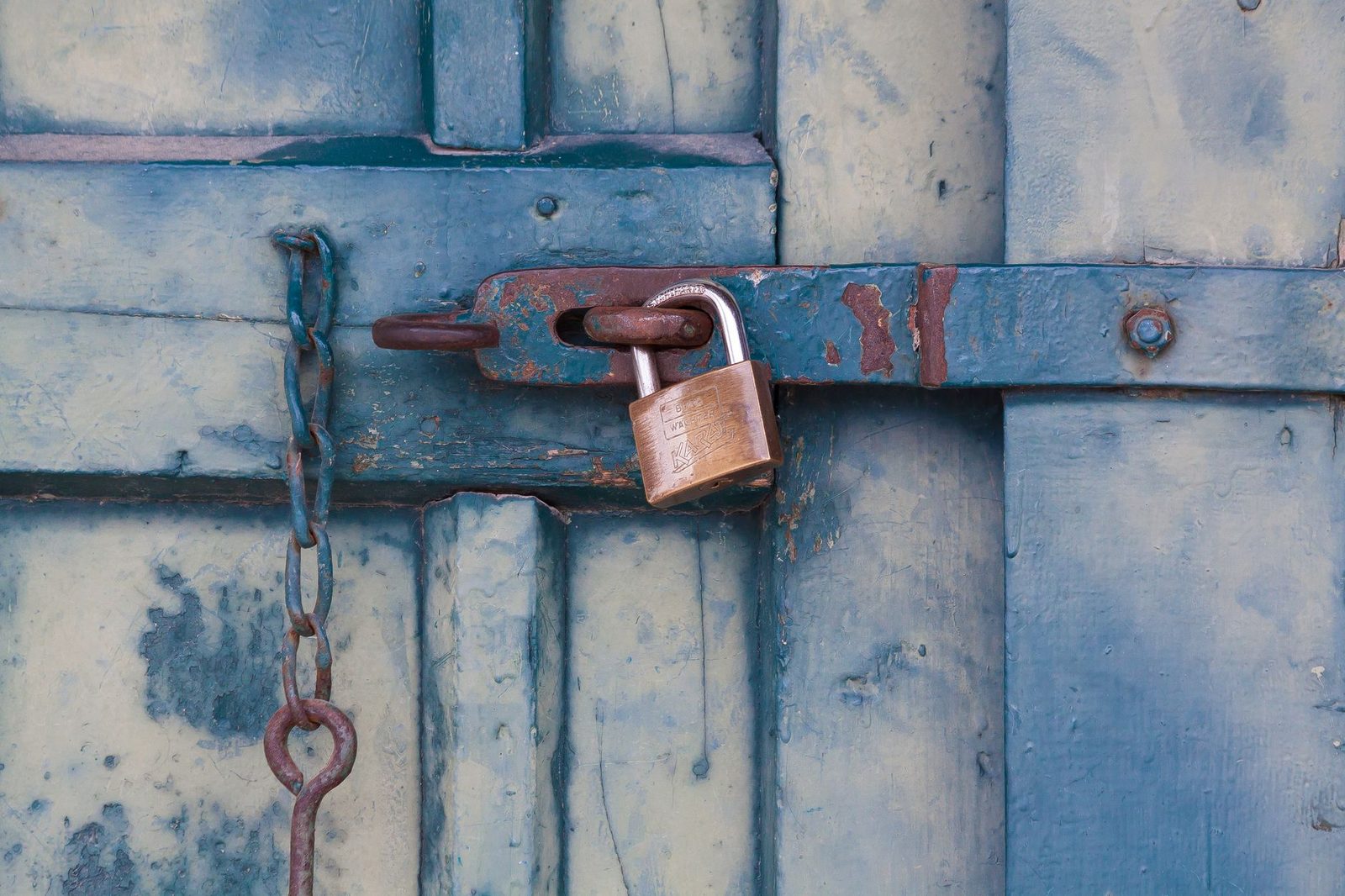 Cadenas en laiton fermé sur un loquet rouillé d'une vieille porte en bois peinte en bleu, avec une chaîne