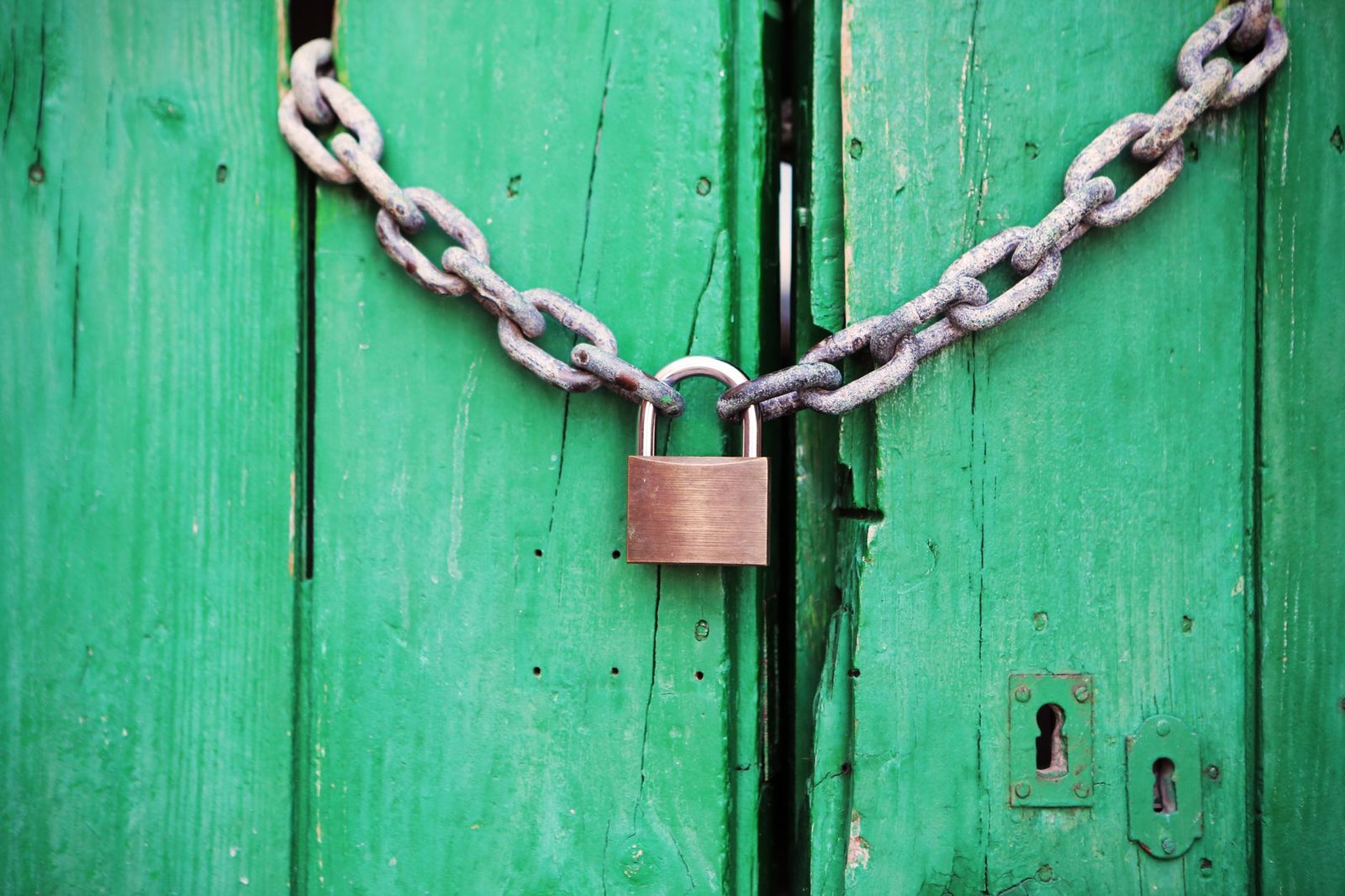Cadenas métallique et chaîne rouillée fermant une porte en bois peinte en vert