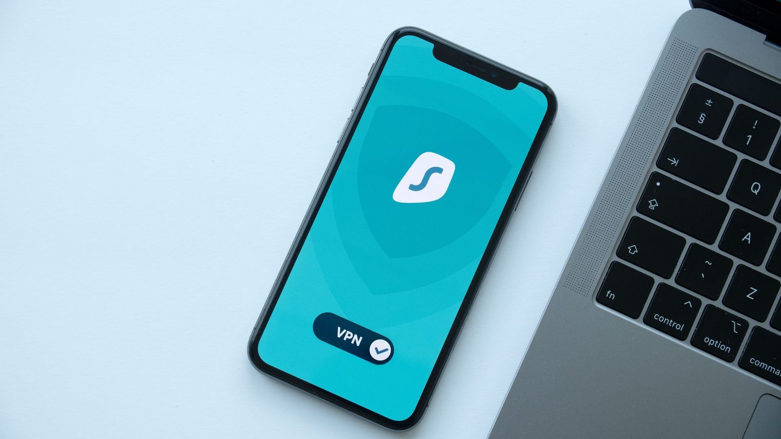 Smartphone posé sur un ordinateur portable affichant une application VPN à l'écran turquoise