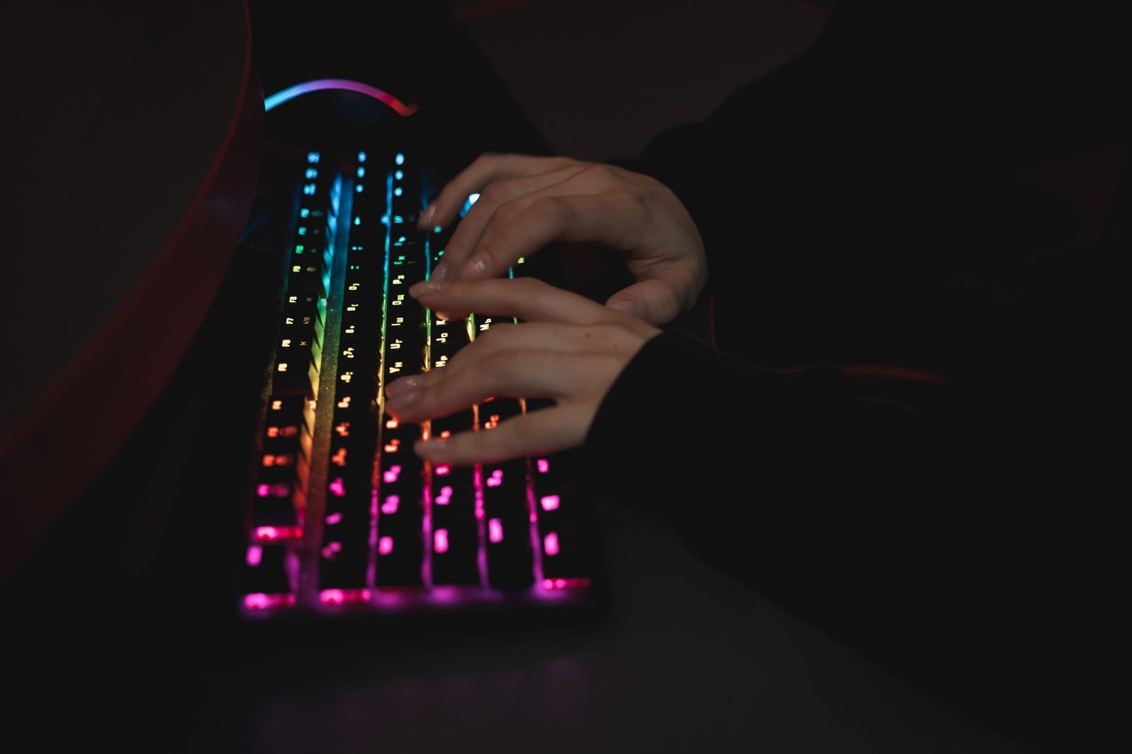 Mains d'une personne tapant sur un clavier rétroéclairé multicolore dans une pièce sombre