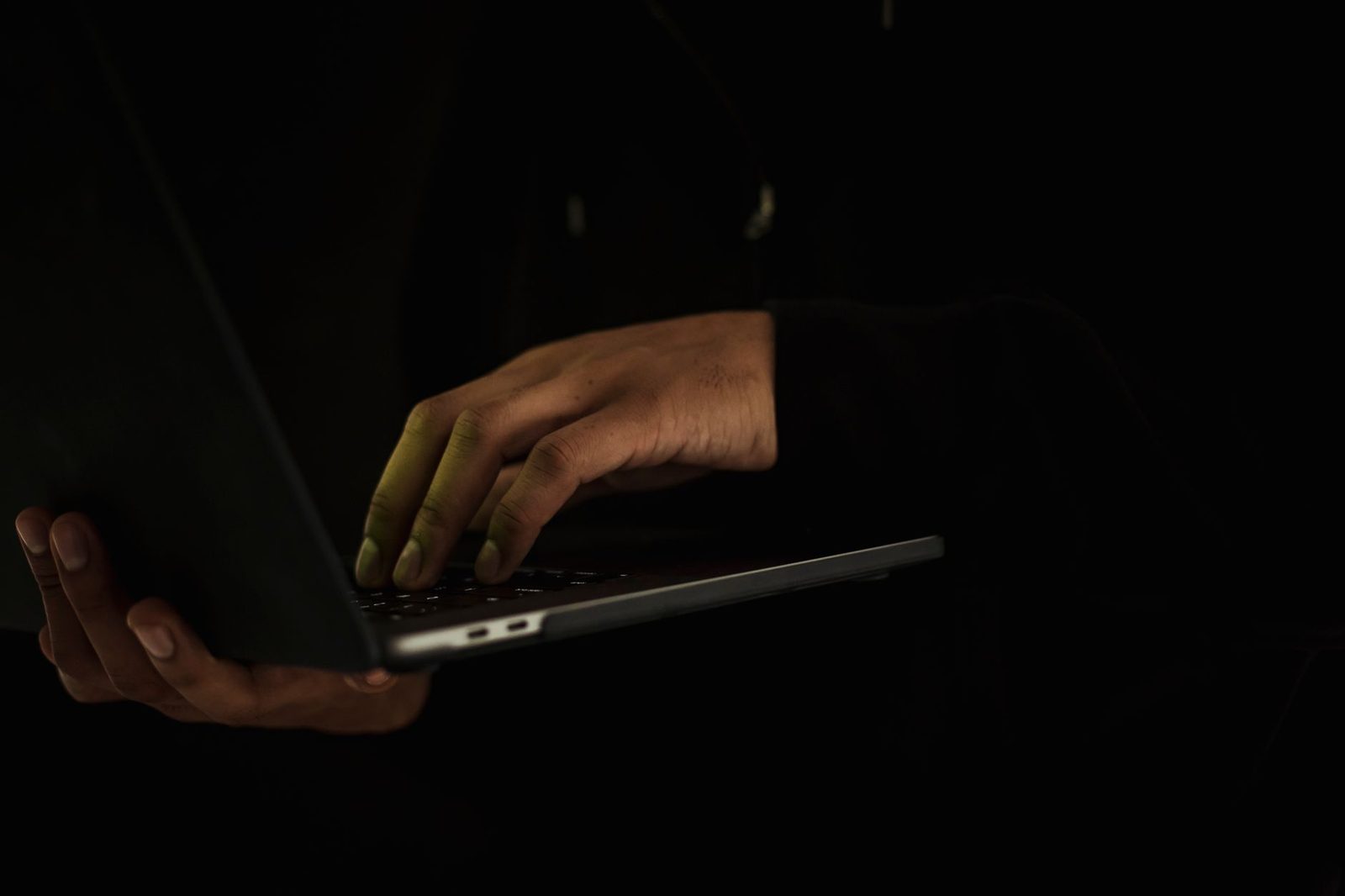 Mains d'une personne tapant sur le clavier d'un ordinateur portable dans l'obscurité
