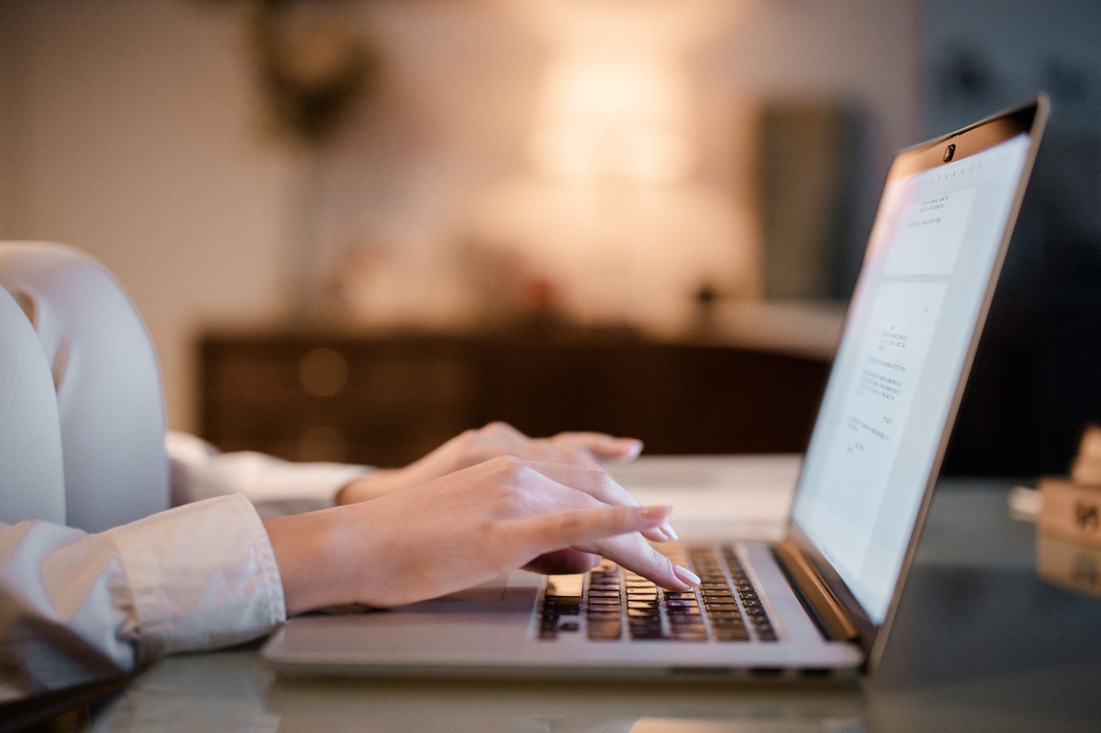 Mains d'une femme tapant sur le clavier d'un ordinateur portable ouvert, dans une pièce sombre