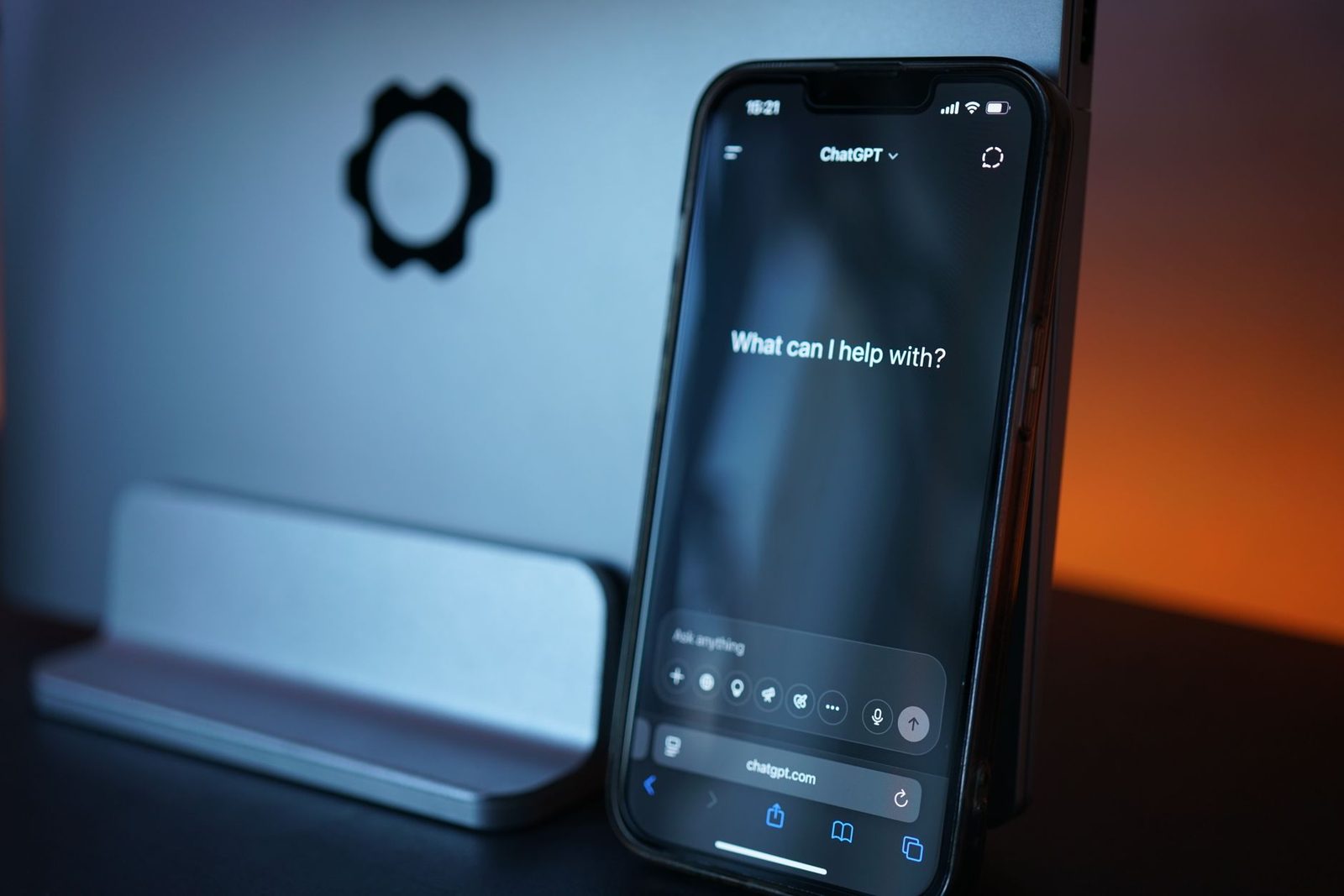 Smartphone affichant l'application ChatGPT posé devant un ordinateur, dans une lumière bleue et orange