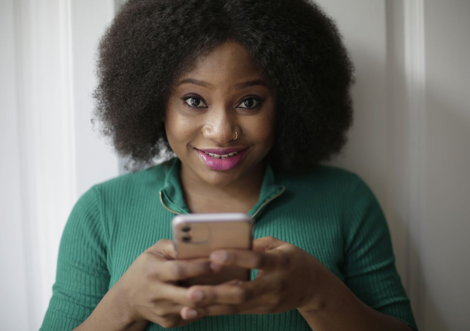 Jeune femme souriante en pull vert tenant un smartphone entre ses mains