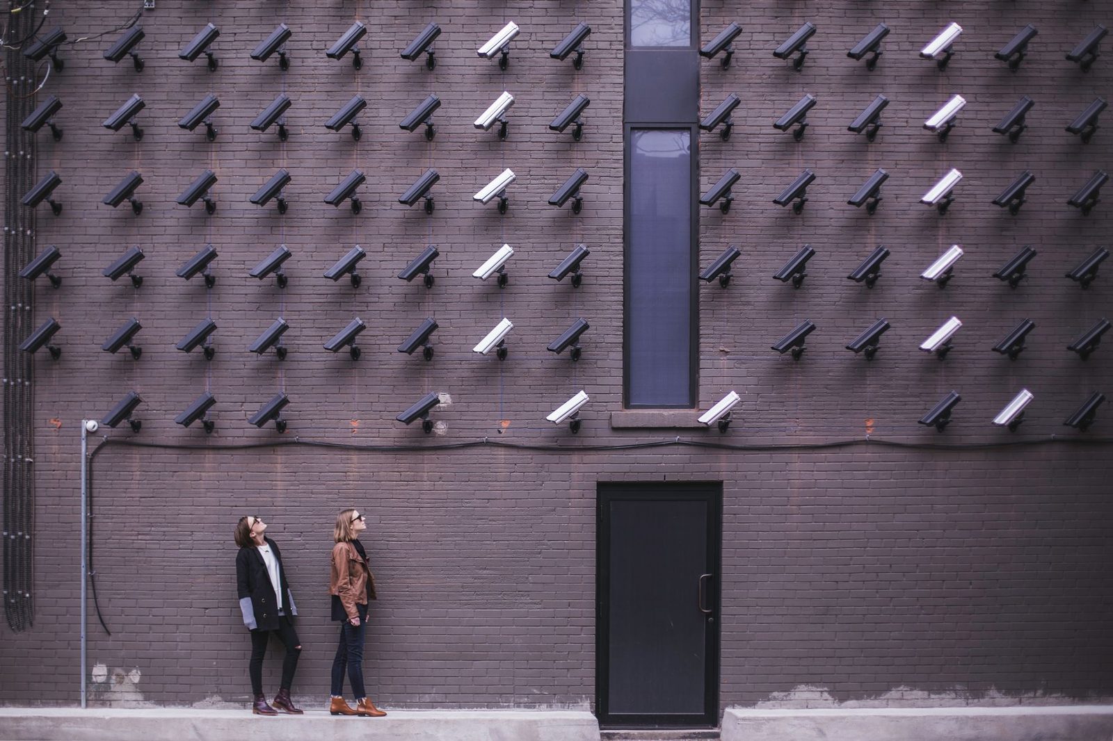 Deux femmes lèvent les yeux vers un mur de briques couvert de dizaines de caméras de surveillance