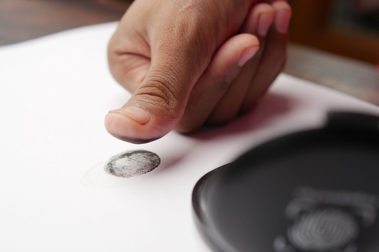 Un doigt posé au-dessus d'une empreinte digitale noire sur une feuille de papier blanc.