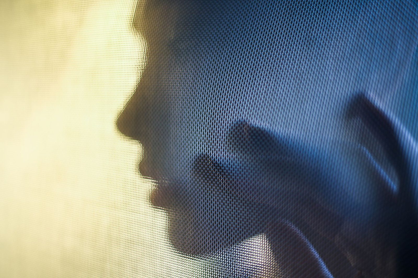 Silhouette d'un visage et d'une main vus à travers un écran ou un voile grillagé