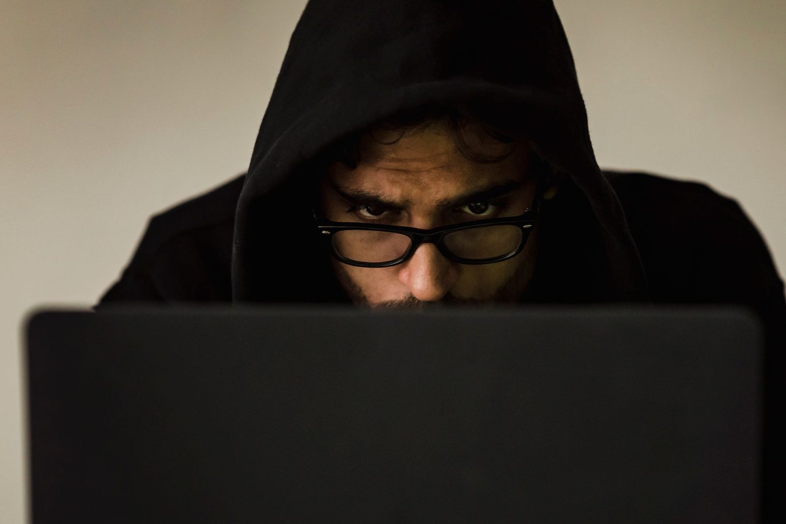 Un homme avec un sweat à capuche noir et des lunettes regardant un ordinateur portable.