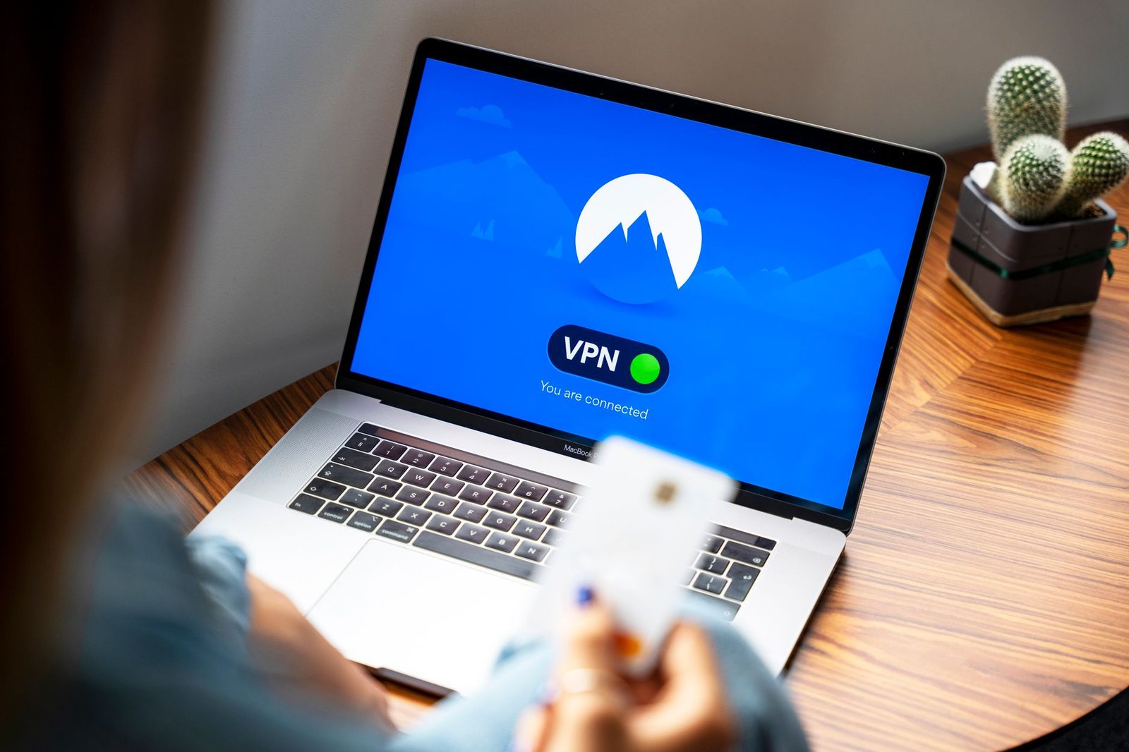 लैपटॉप के सामने बैठी महिला जिसकी स्क्रीन पर कनेक्टेड VPN दिख रहा है, हाथ में बैंक कार्ड