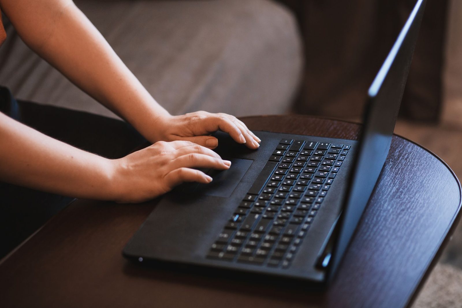 Mains d'une personne tapant sur le clavier d'un ordinateur portable noir posé sur une table en bois