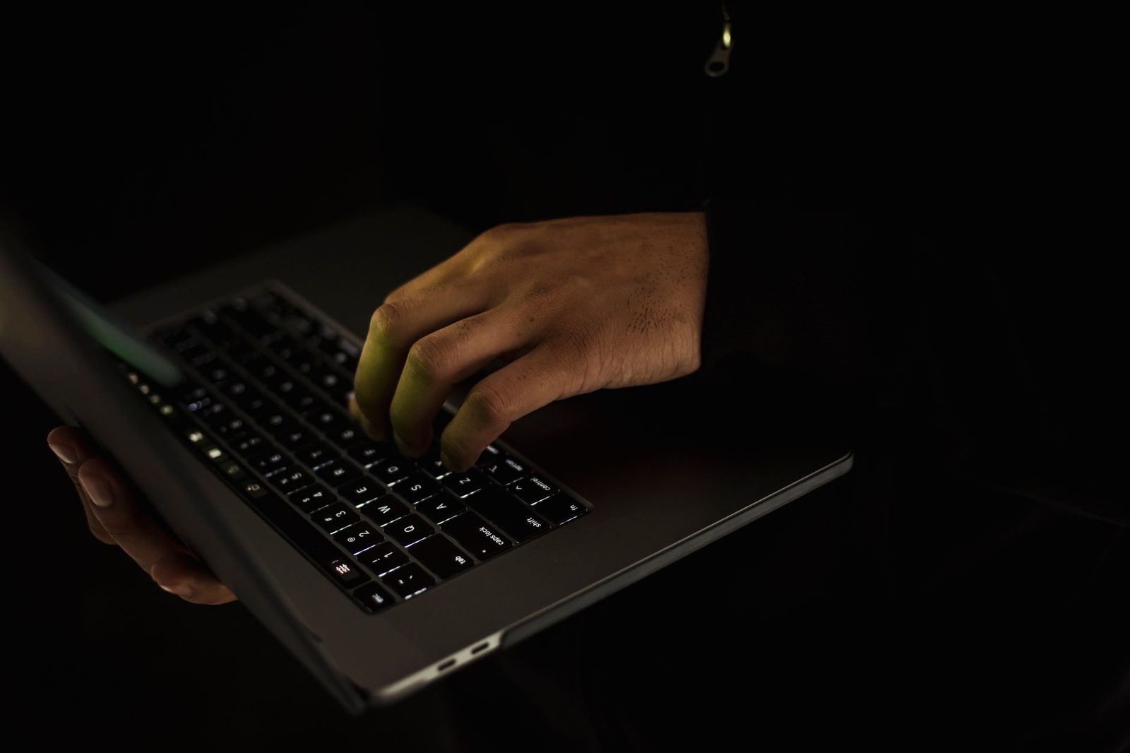 Main d'une personne tapant sur le clavier d'un ordinateur portable dans l'obscurité