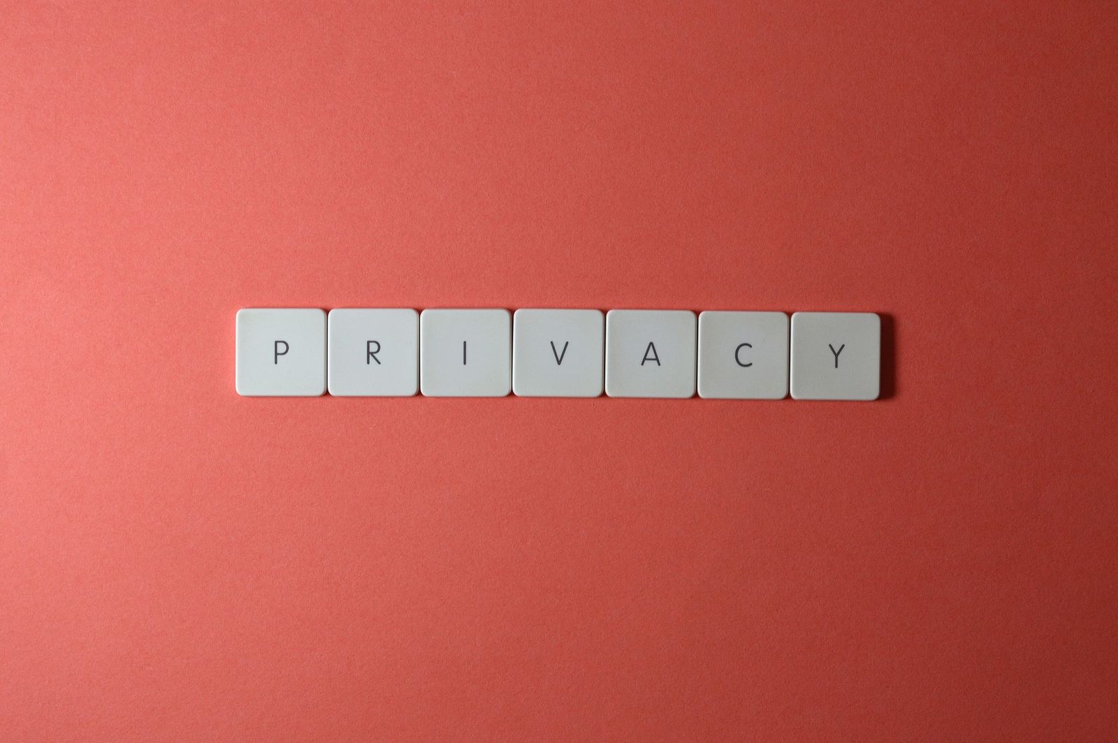 Tuiles blanches formant le mot « privacy » sur un fond rouge corail uni