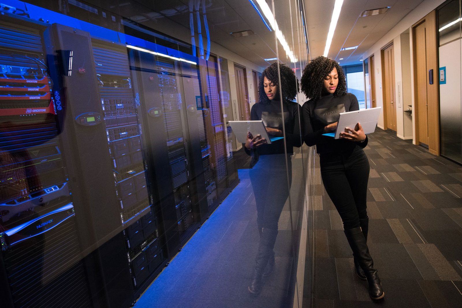 Woman looking at a laptop in a glass-walled corridor running alongside data centre server racks