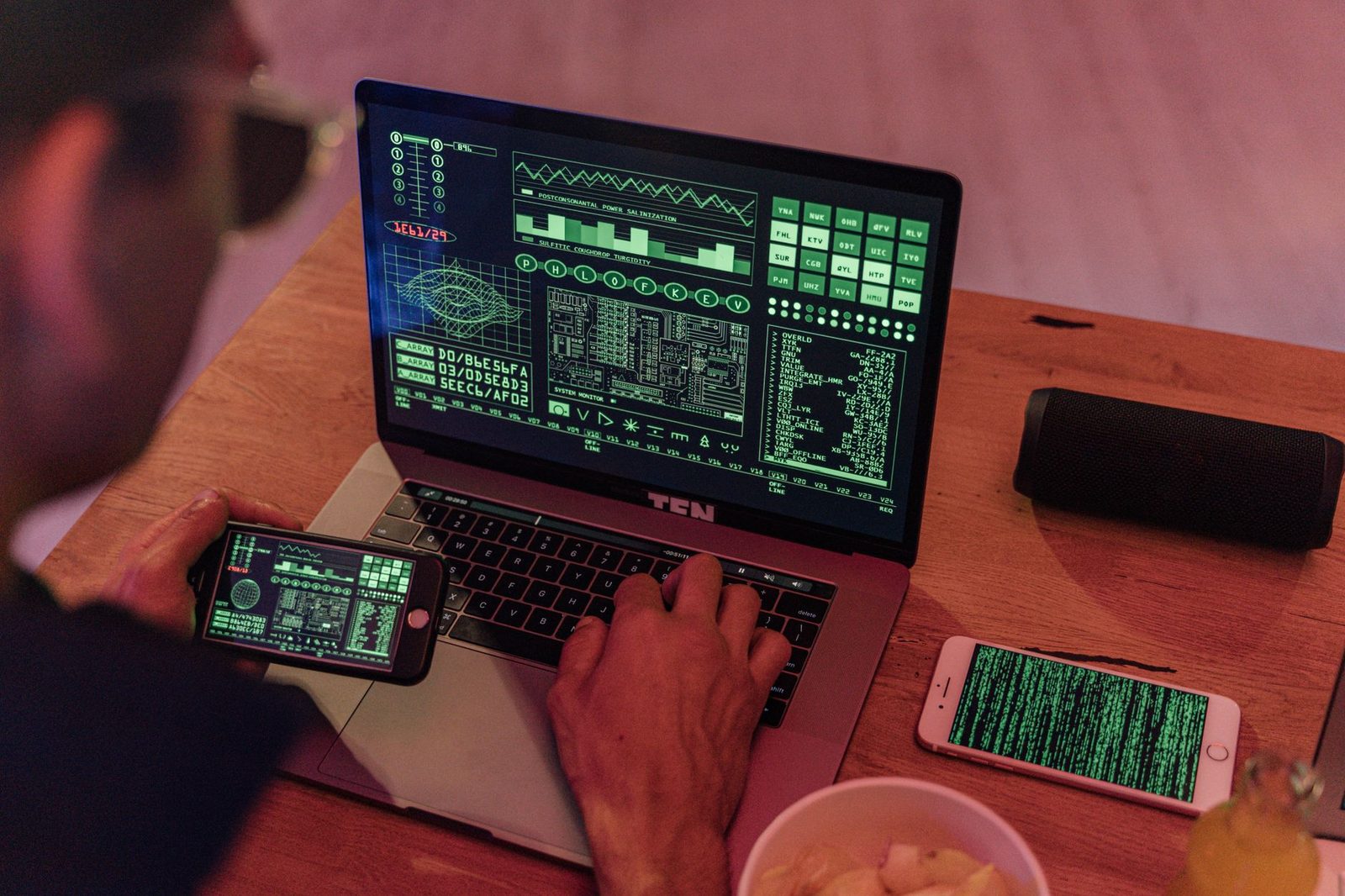 Uomo che digita su un computer portatile con dati verdi sullo schermo, smartphone con un codice a display