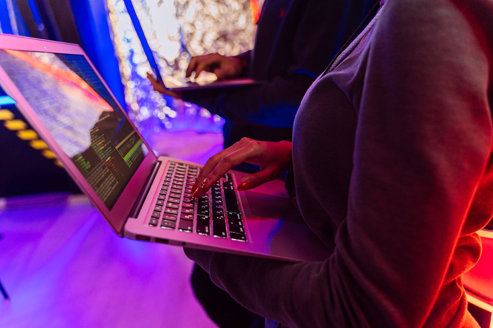 Mani di una persona che digitano su un computer portatile con del codice sullo schermo, sotto una luce al neon viola