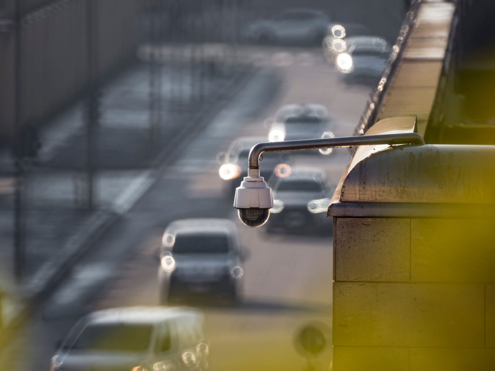 Kuppelförmige Überwachungskamera an einer Brücke über einer Straße mit unscharfen Autos