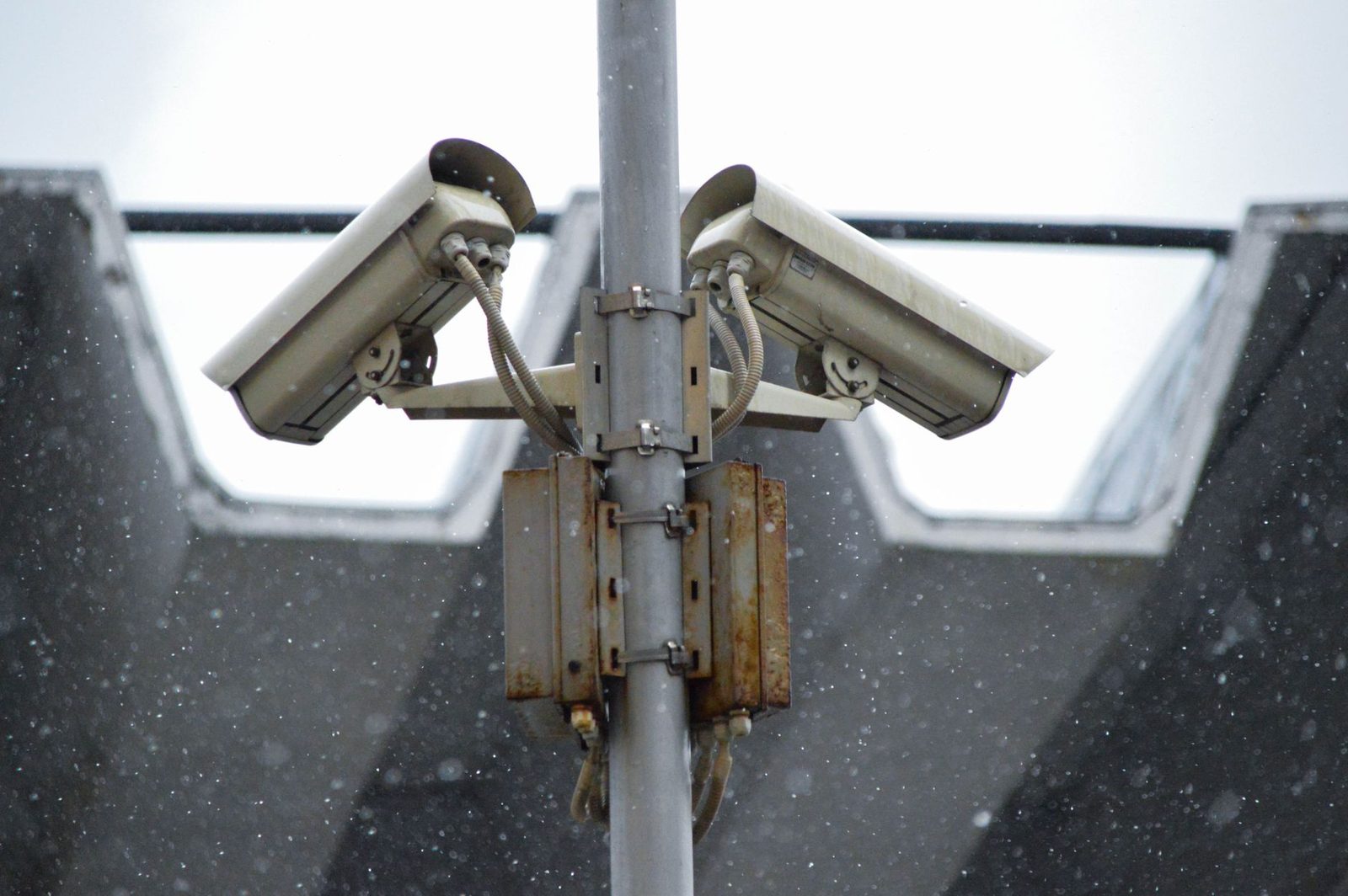Zwei Überwachungskameras an einem Metallmast vor einem Dach, im Schnee