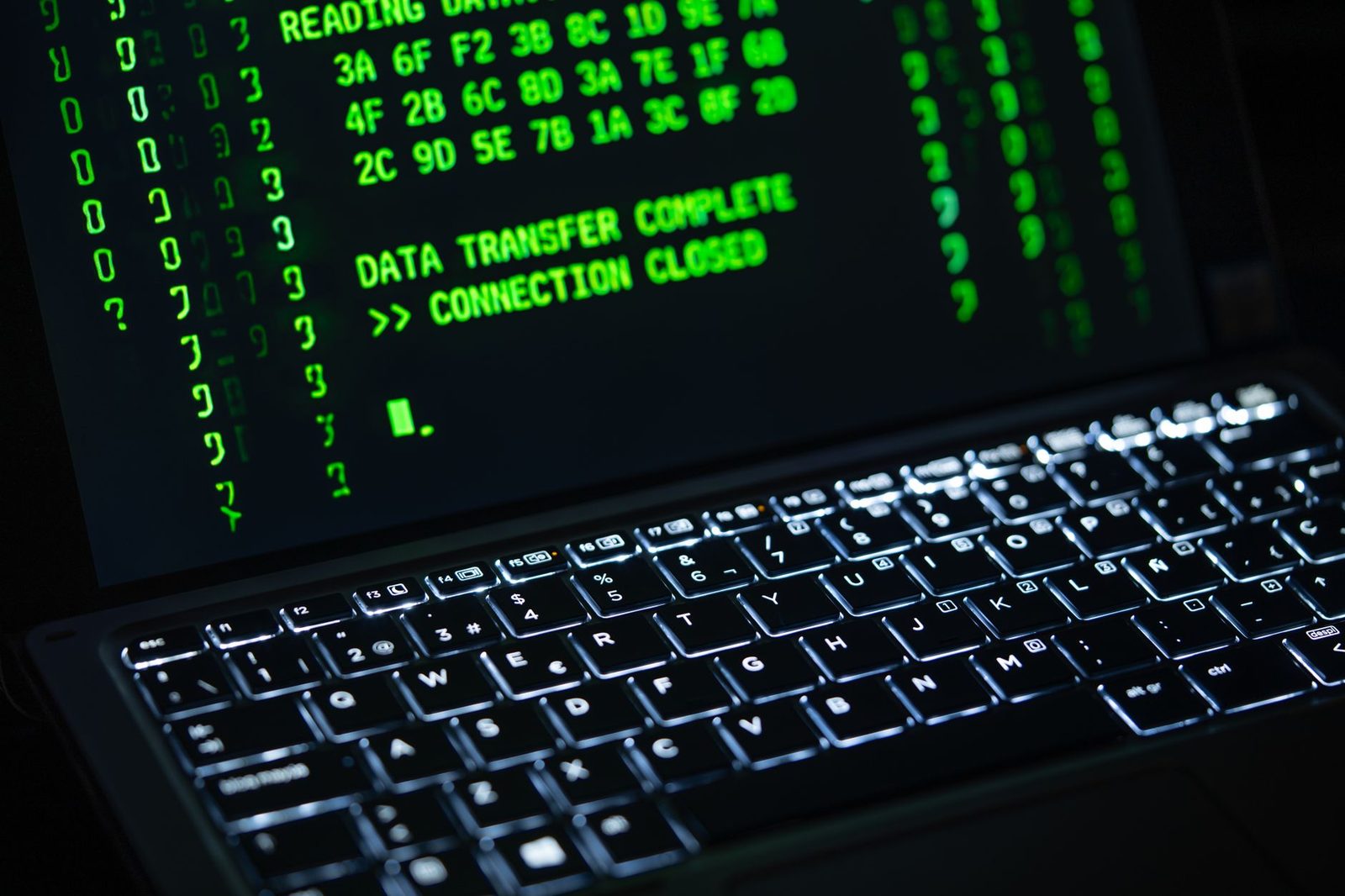 Schermo di un computer portatile che mostra codice verde su sfondo nero sopra una tastiera retroilluminata