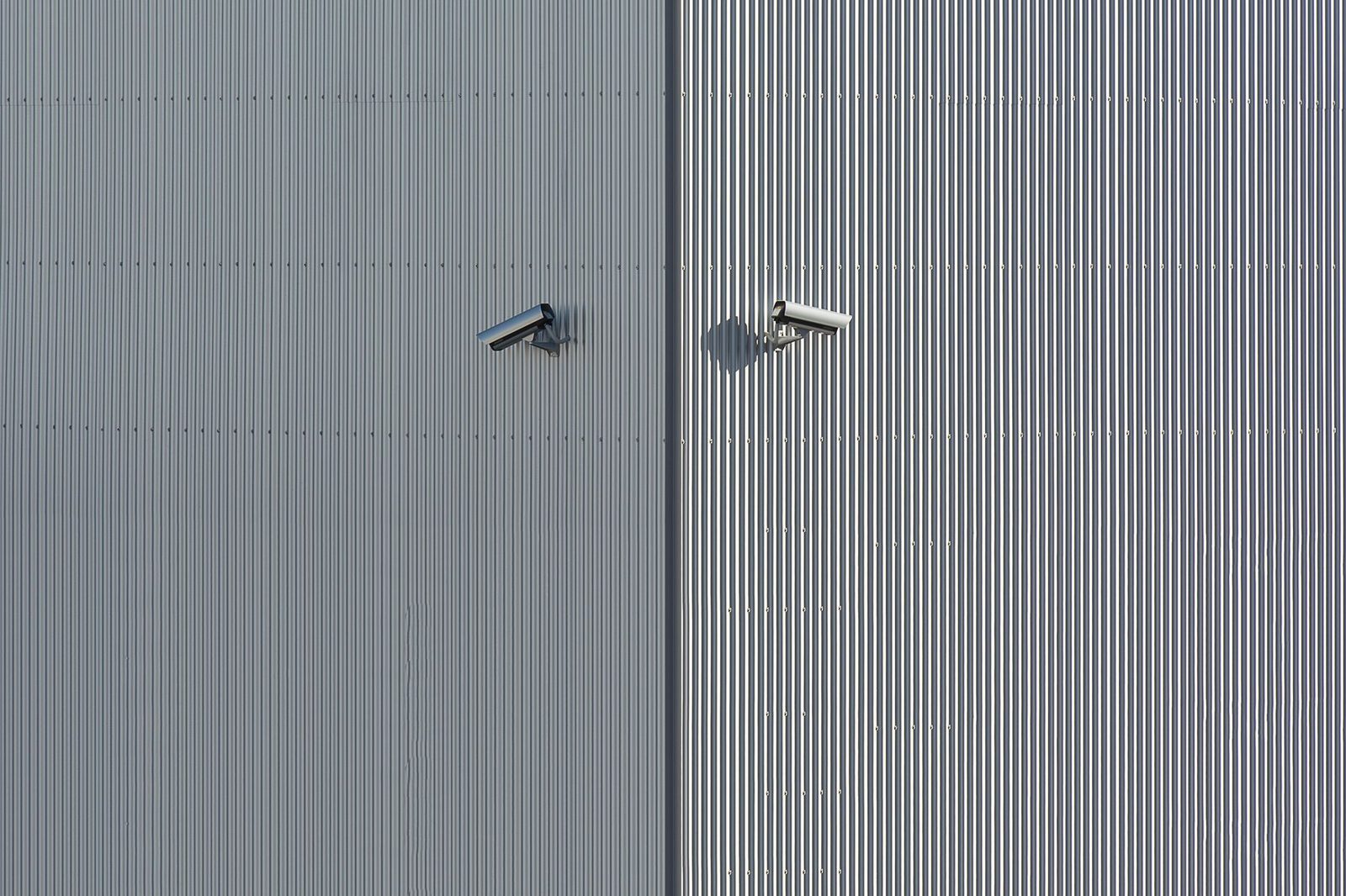Deux caméras de vidéosurveillance fixées sur une façade métallique nervurée grise et blanche