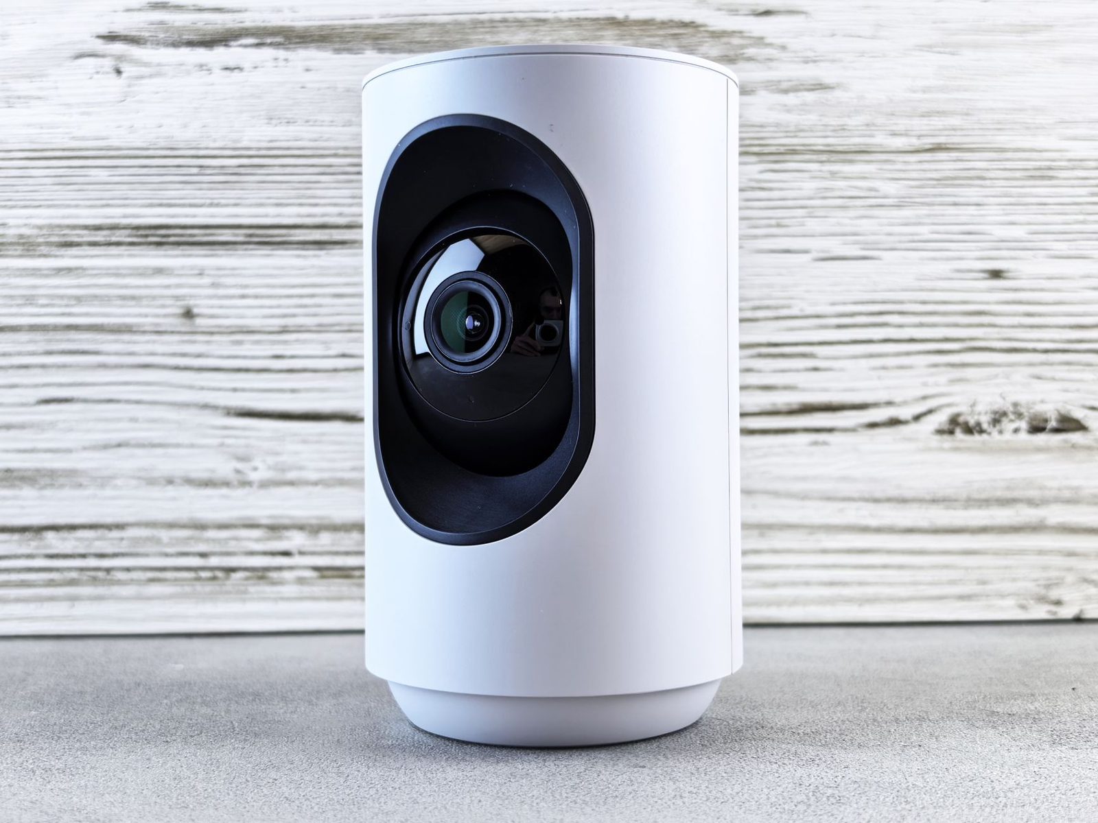 Caméra de surveillance connectée blanche posée devant un mur en bois clair