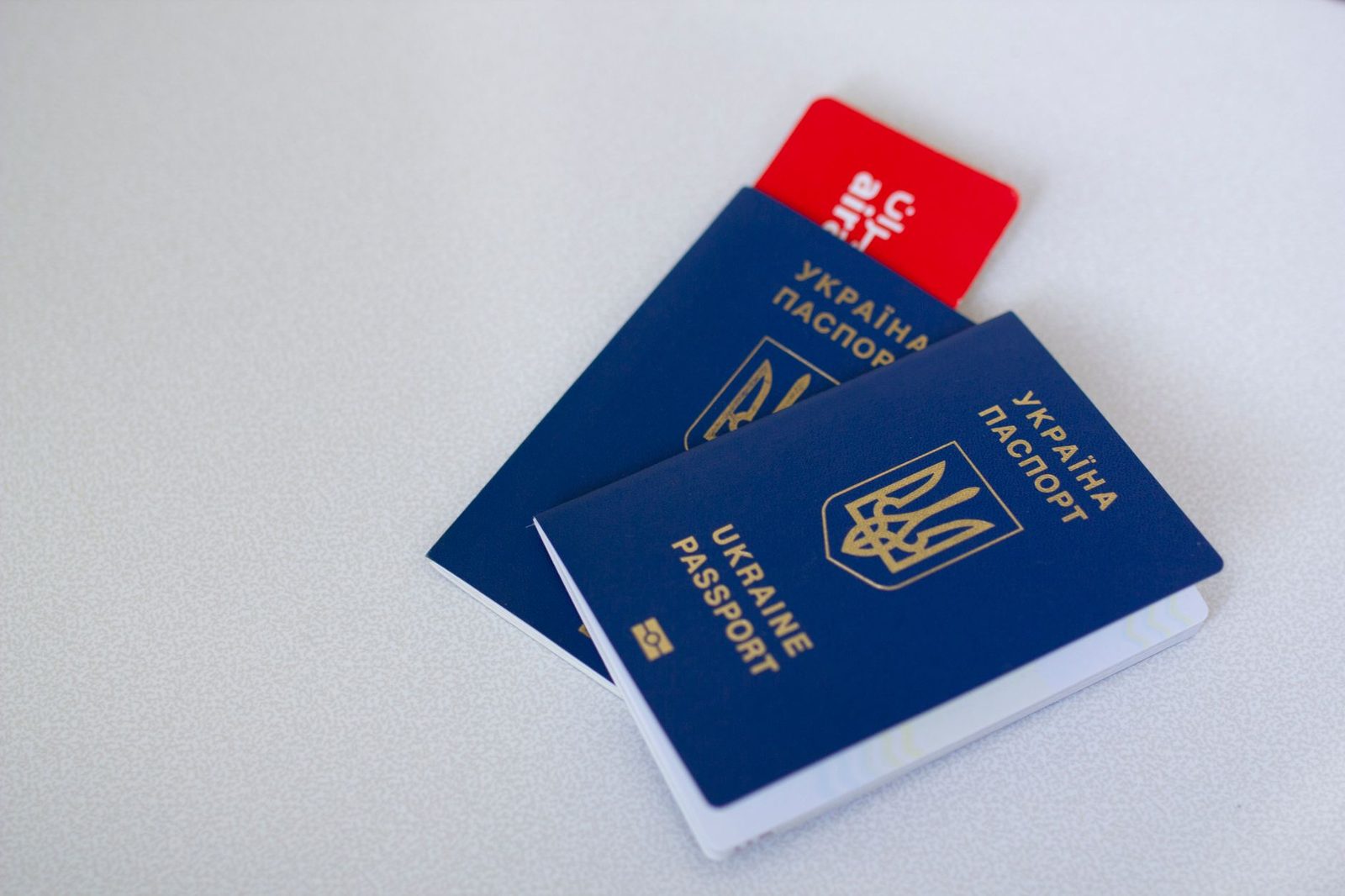 Два синих украинских биометрических паспорта и красная карточка на белой поверхности