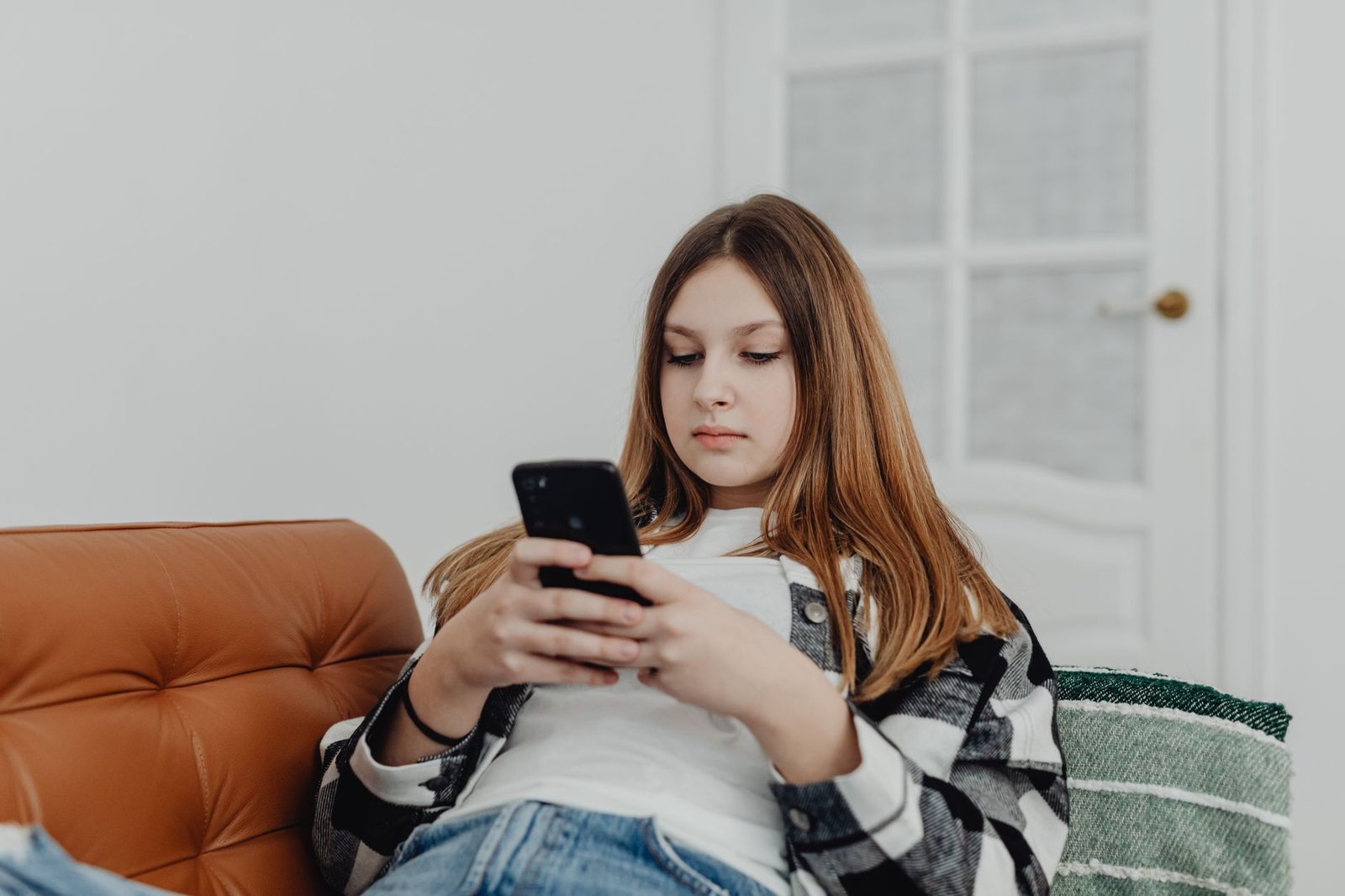 Adolescente assise sur un canapé en cuir, consultant un smartphone dans un salon clair