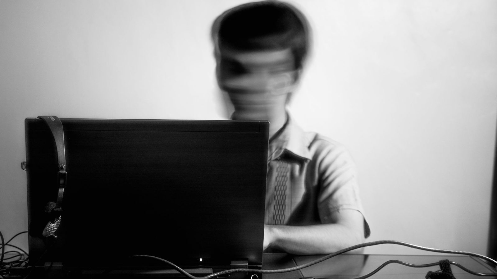 Black and white photo of a person with a blurred face sitting behind a laptop