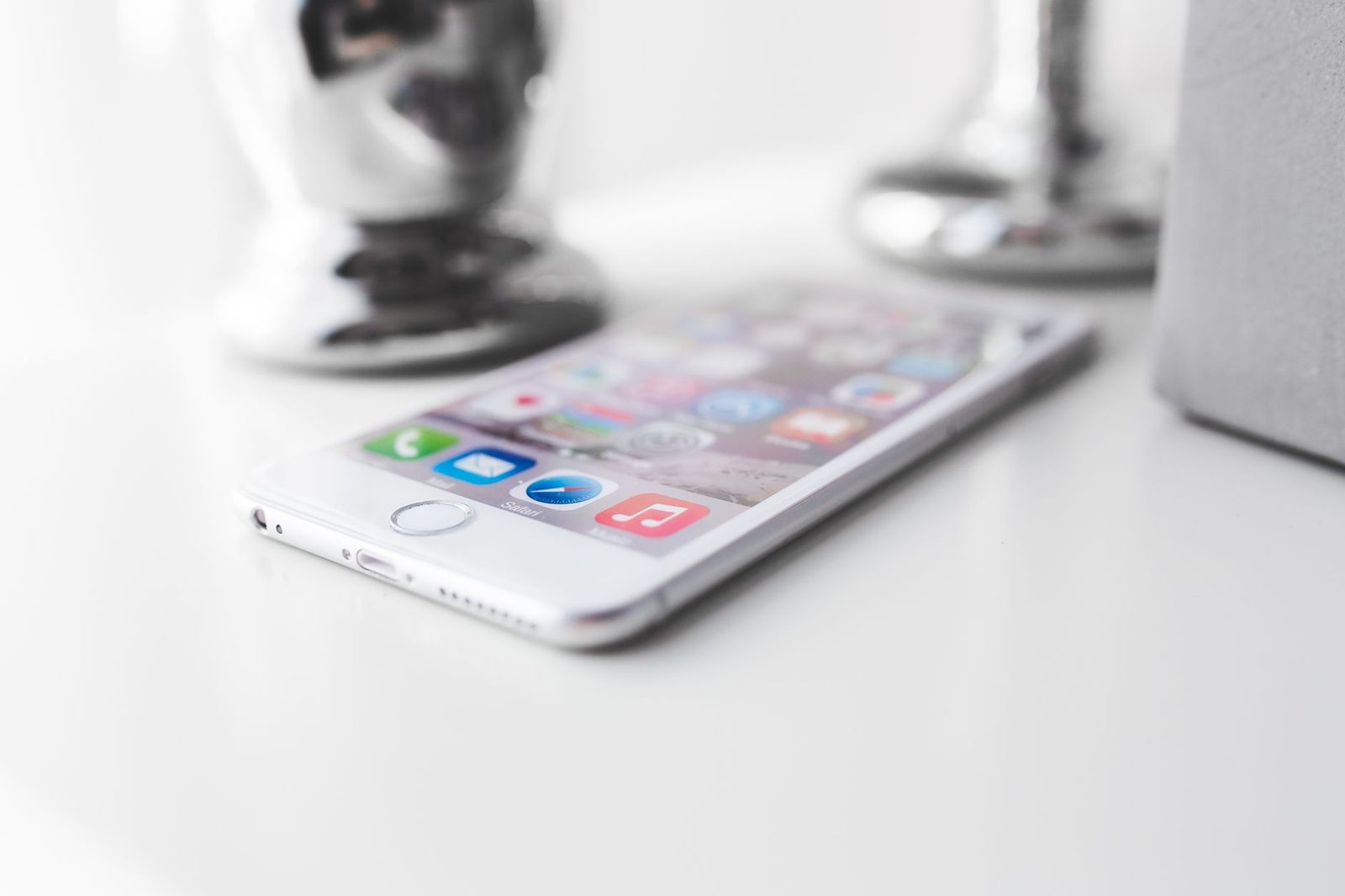 iPhone blanc posé à plat sur une surface claire, écran d'accueil iOS allumé avec ses icônes d'applications