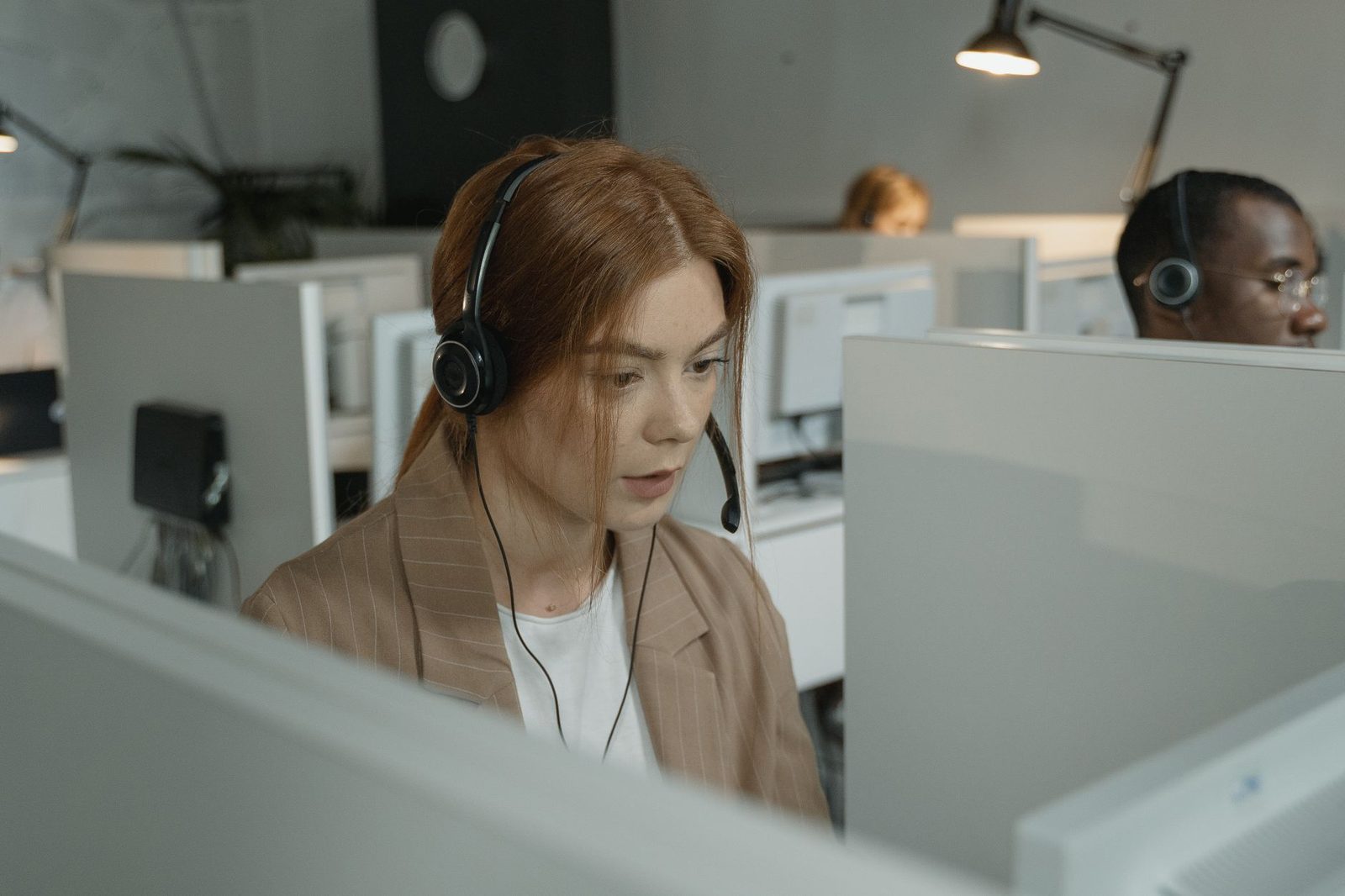 Téléopératrice avec casque audio devant un écran dans un centre d'appels, collègues en arrière-plan