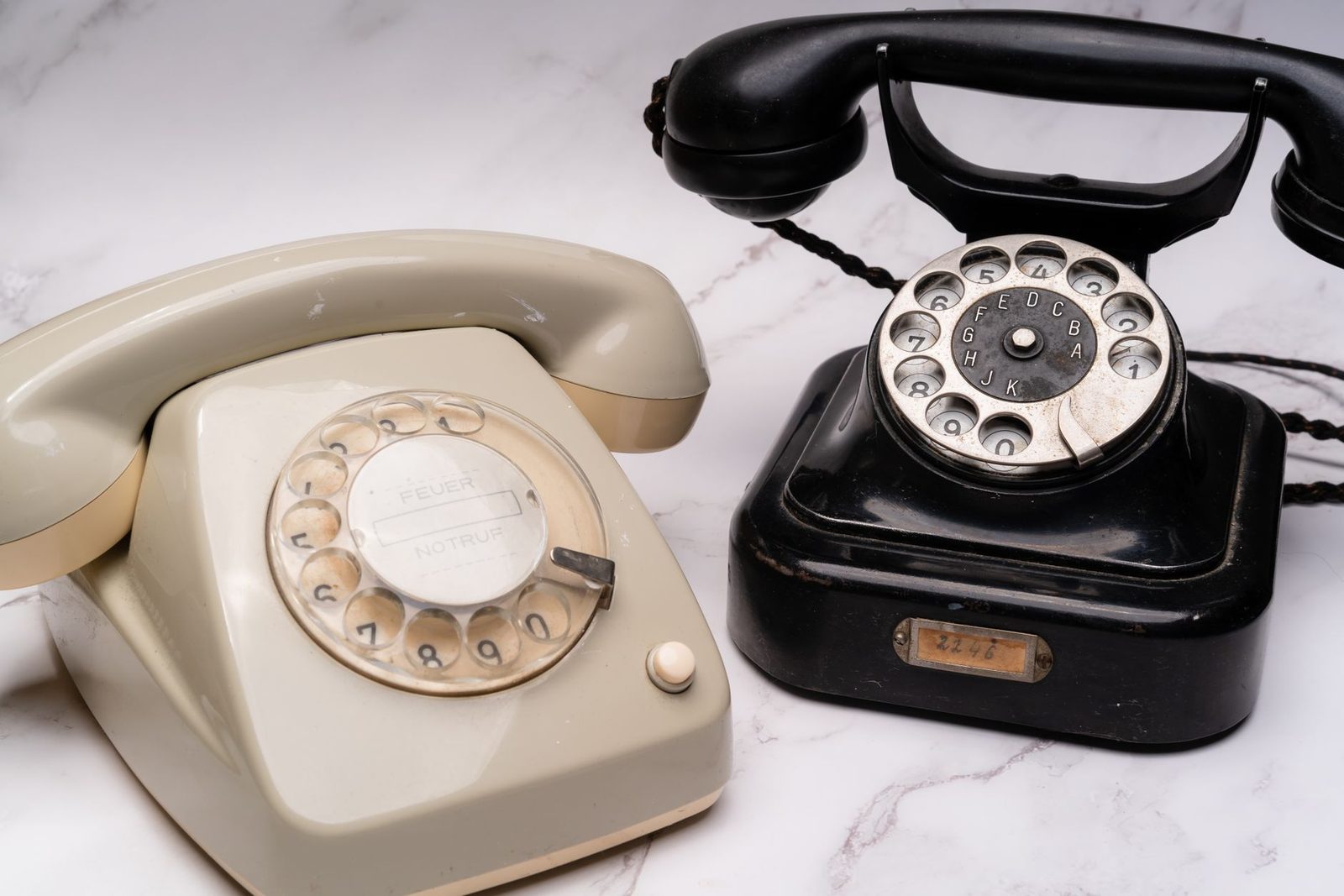 Two vintage rotary phones, one beige and one black, sitting on a white marble surface