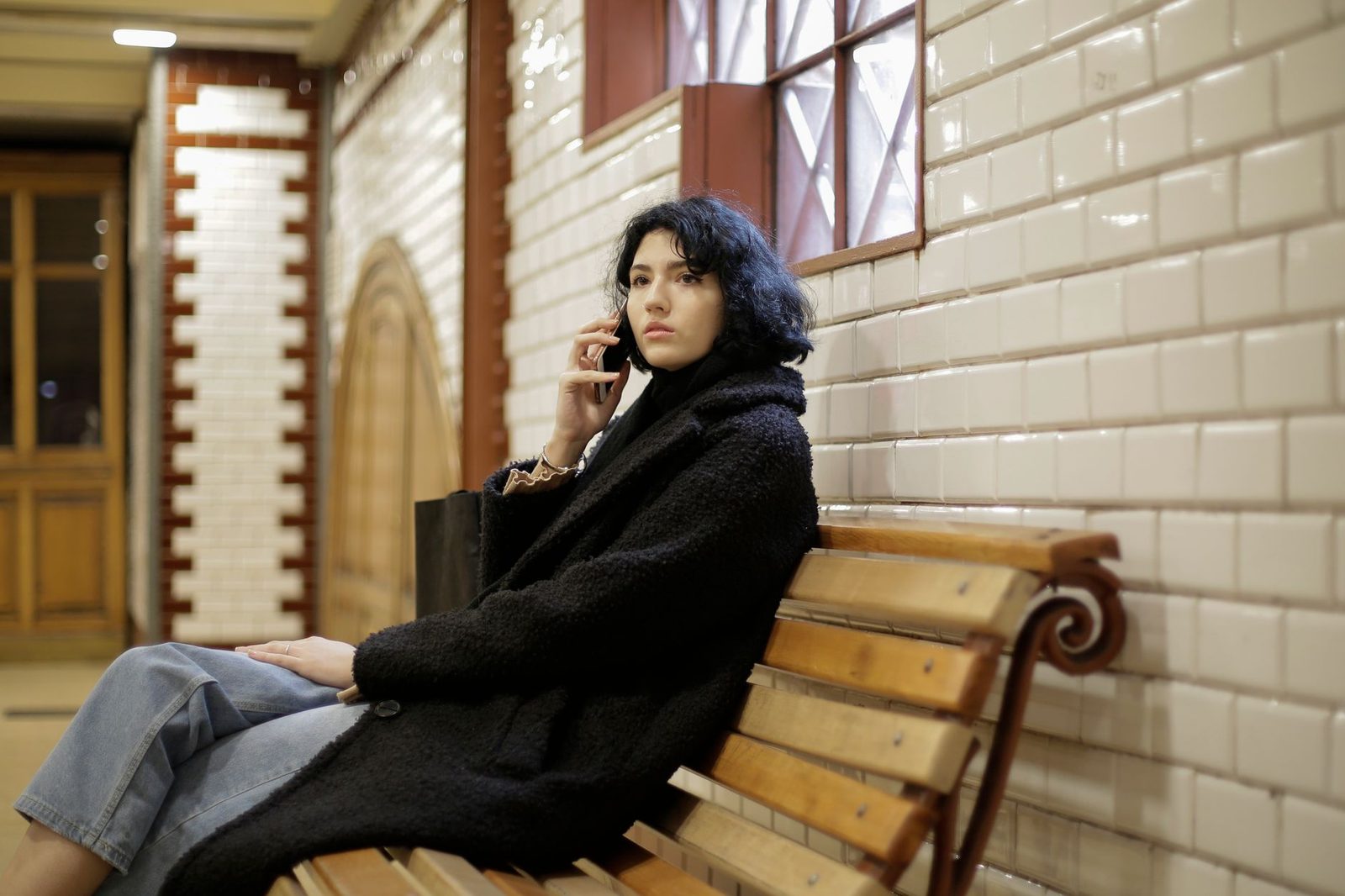 Young woman in a black coat sitting on a bench, mobile phone to her ear, looking annoyed