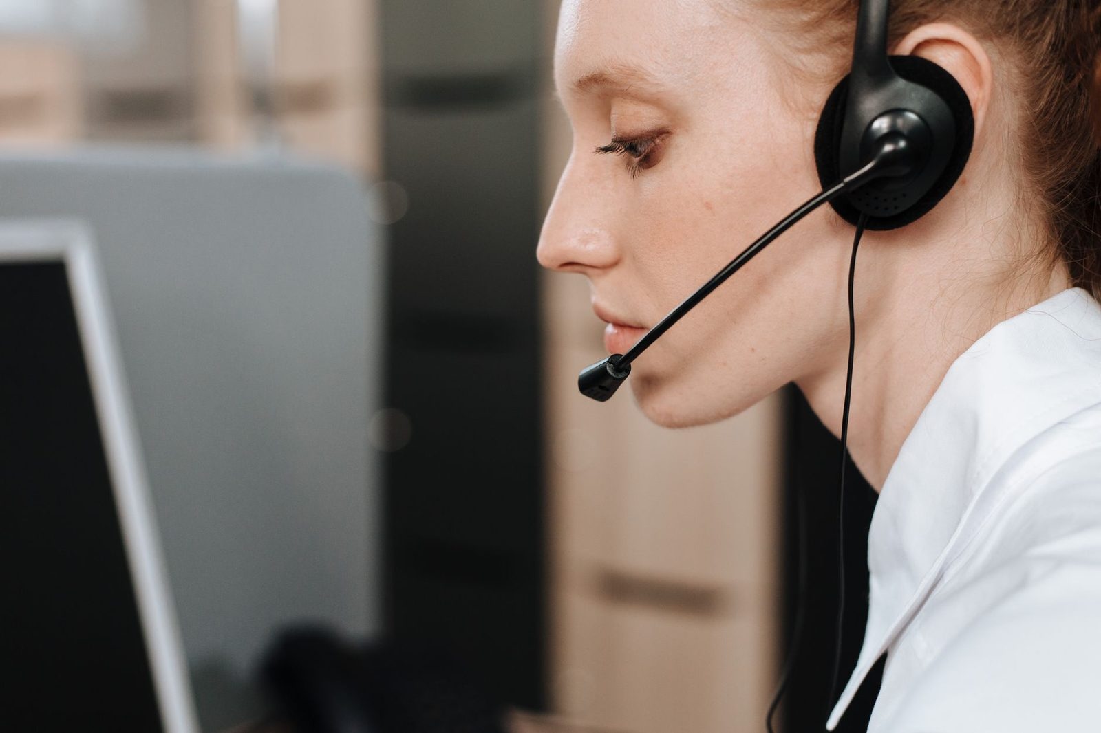 Young woman in profile wearing a headset in front of a computer screen in a call centre