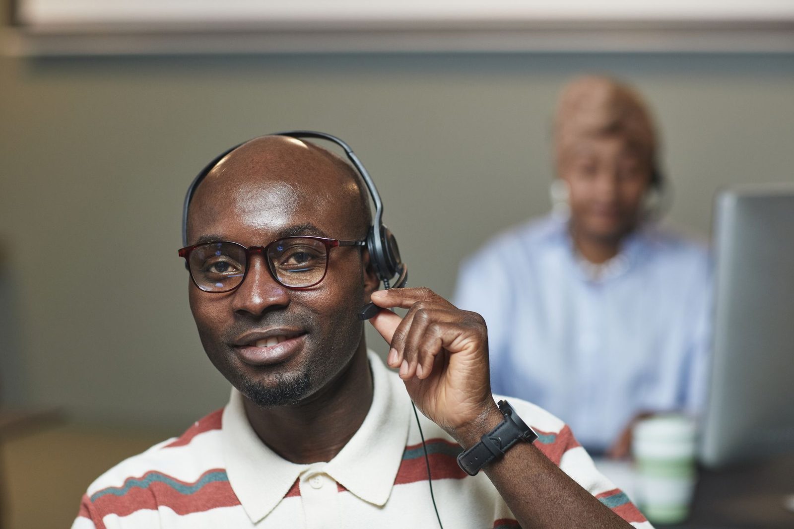 Homme à lunettes portant un casque-micro dans un centre d'appels, collègue floue en arrière-plan