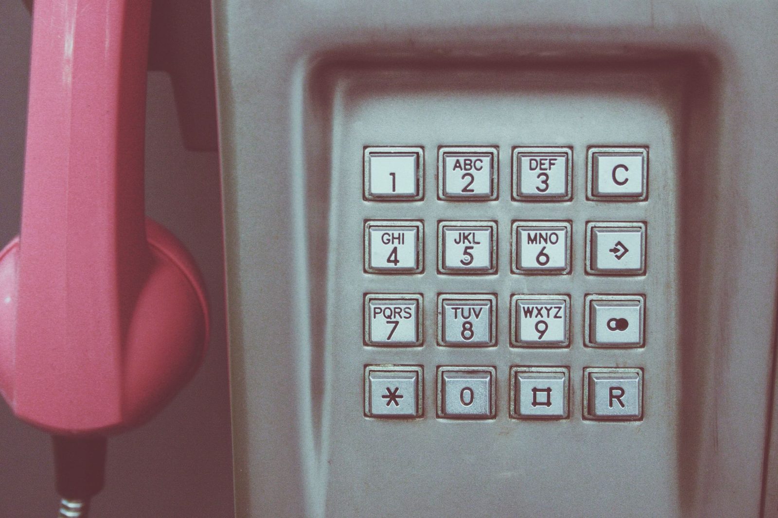 Gros plan sur le clavier d'un téléphone public gris avec un combiné rose accroché à gauche
