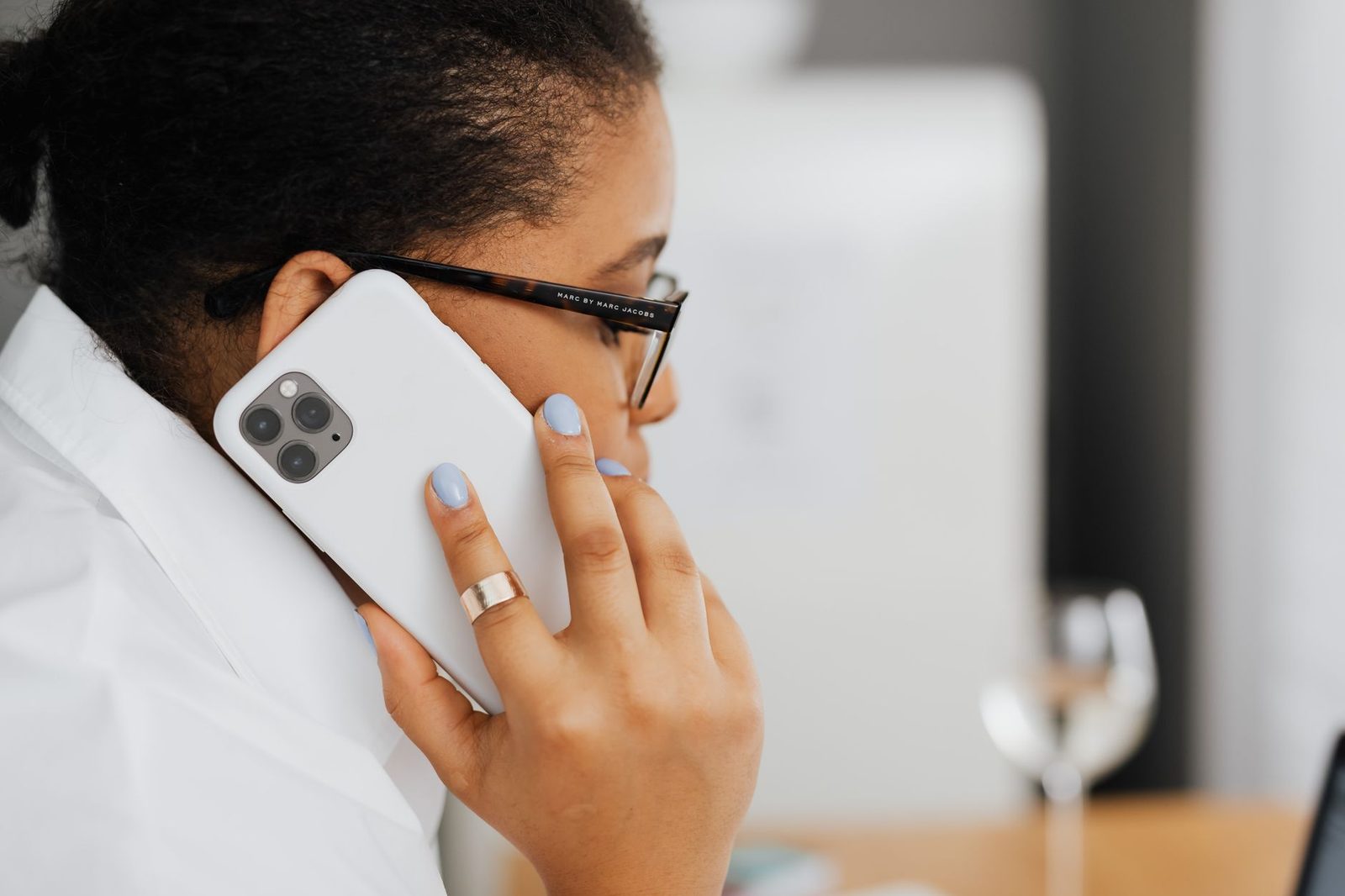 Femme à lunettes passant un appel avec un smartphone blanc tenu contre son oreille