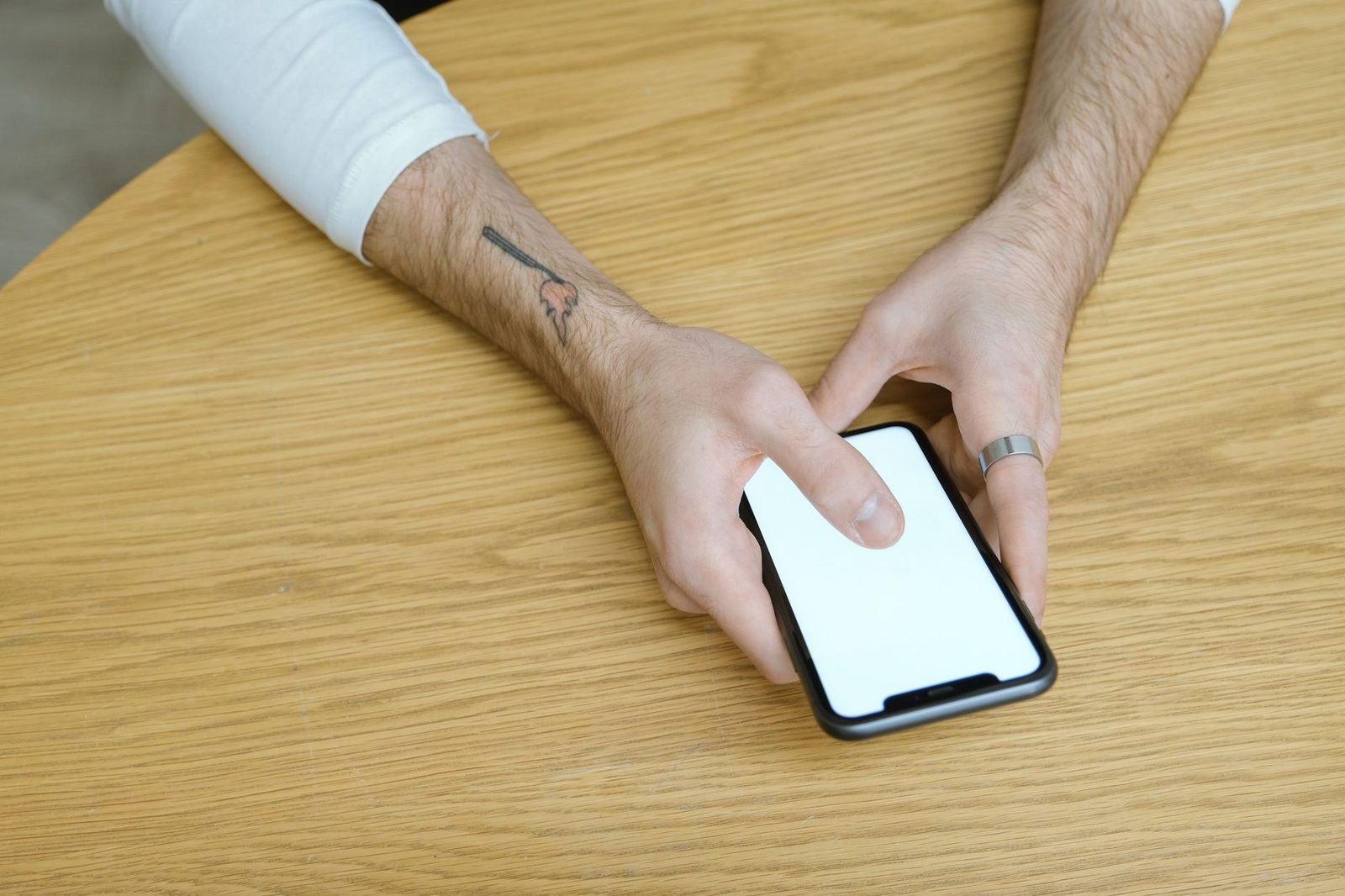 A man's hands holding a smartphone with a white screen resting on a wooden table