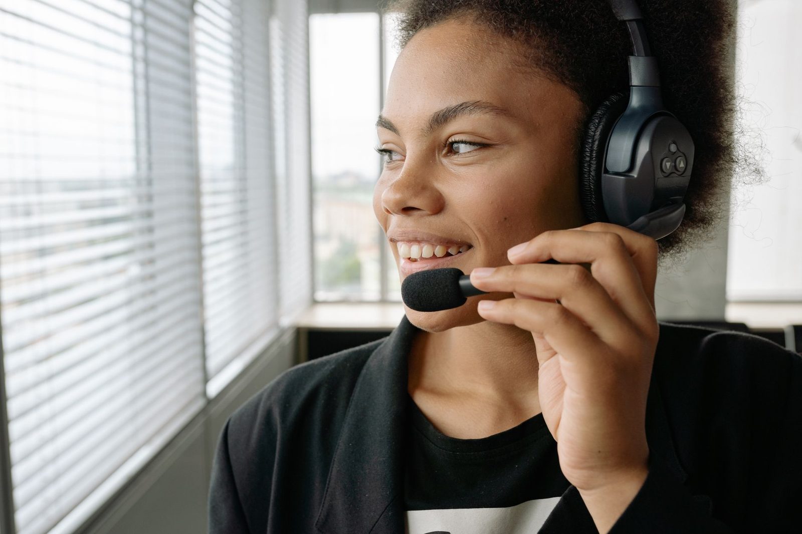 Smiling young woman wearing a call-centre headset in an office, near a window with blinds