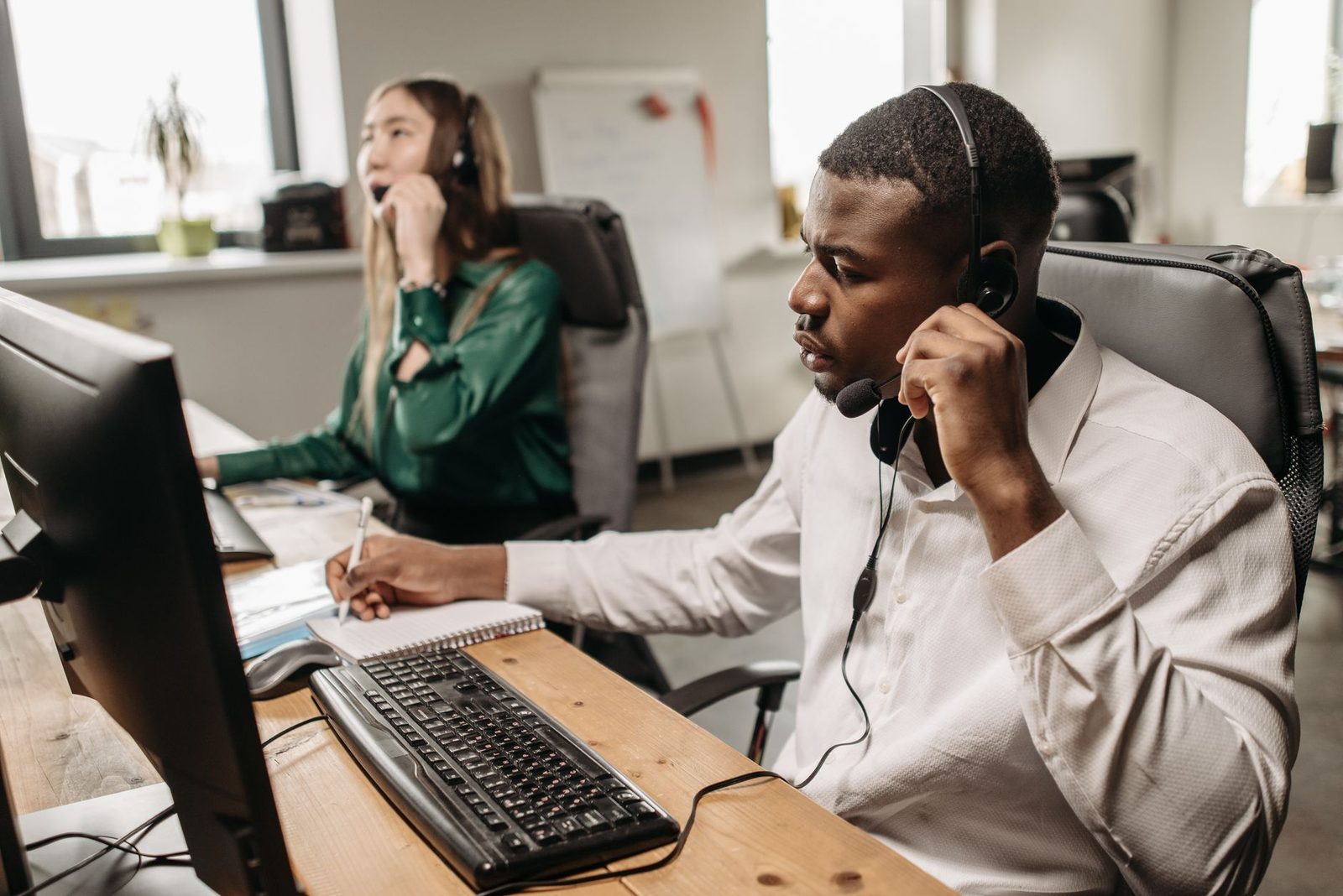 Two call-centre agents wearing headsets in front of computers and a keyboard