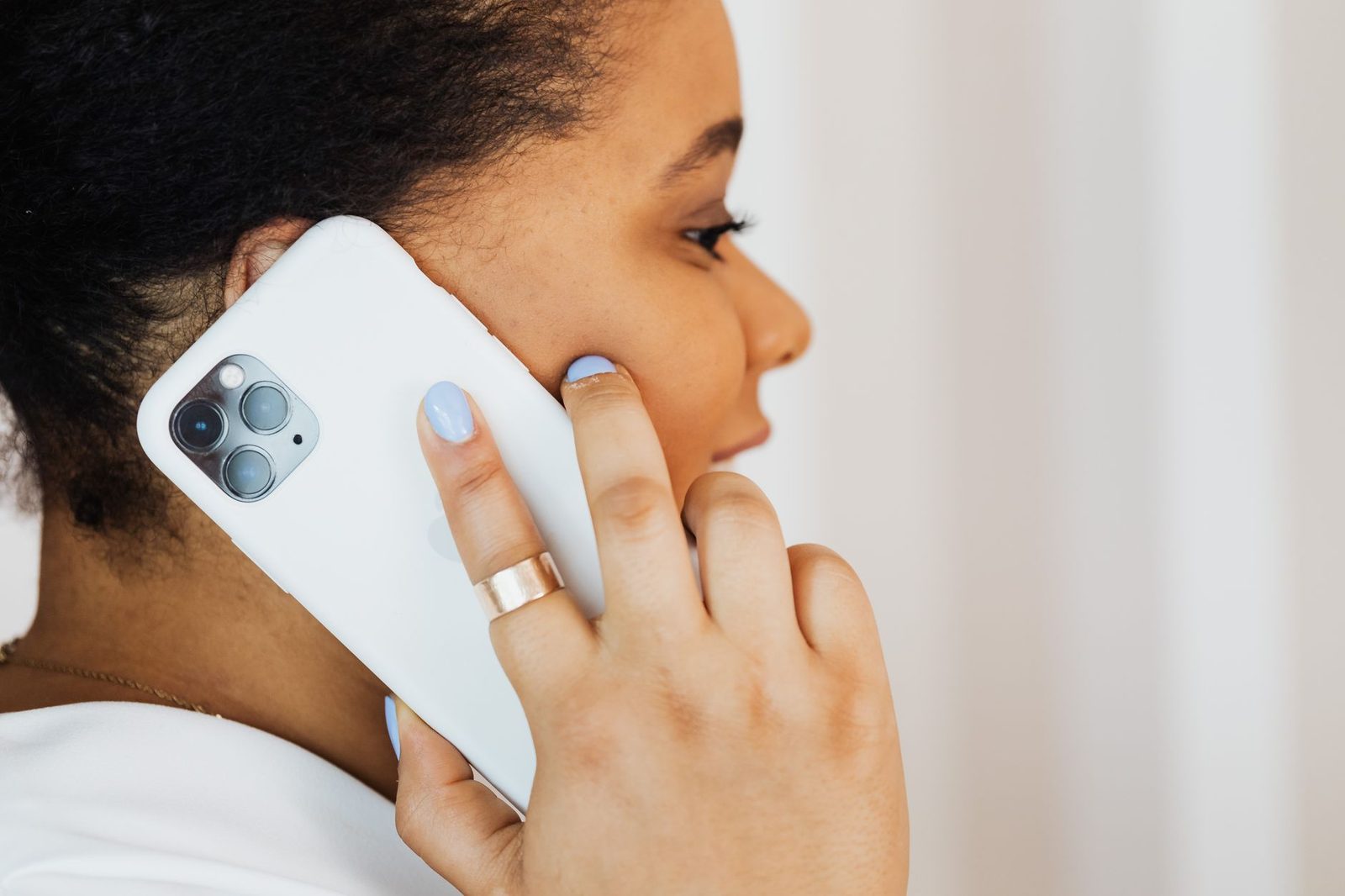 Jeune femme de profil tenant un smartphone blanc contre son oreille lors d'un appel téléphonique