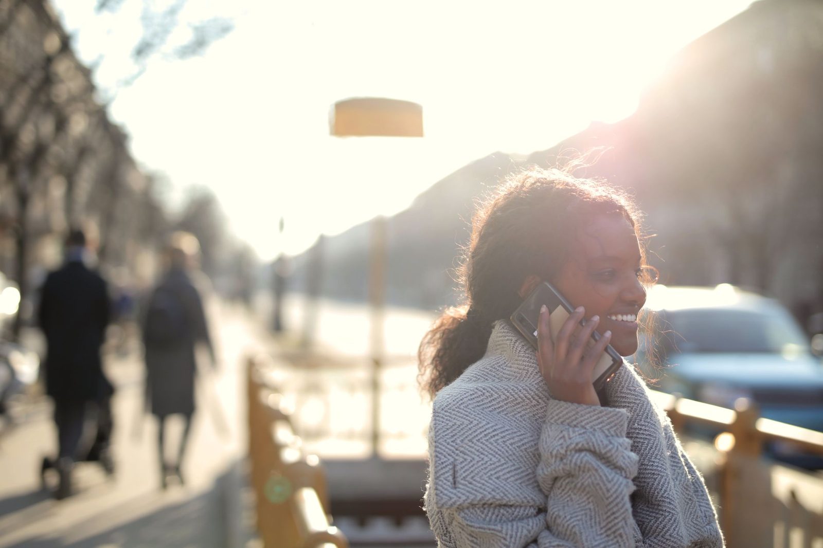 Femme souriante passant un appel sur son téléphone portable dans une rue ensoleillée
