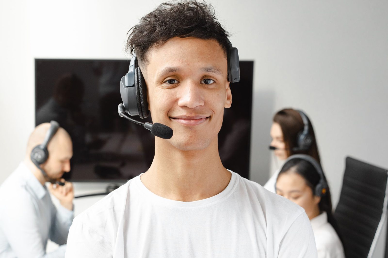 Smiling young man wearing a headset in a call centre, colleagues in the background