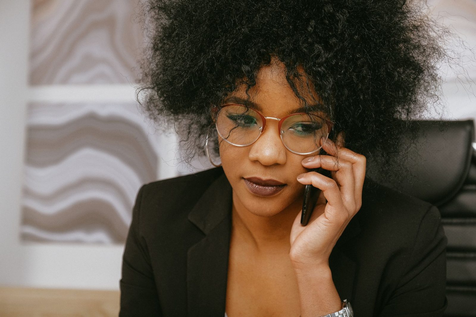 Woman in glasses and a black jacket making a call with a mobile phone to her ear, looking worried